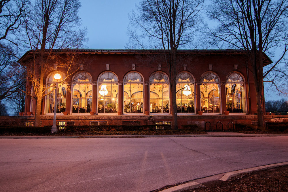 Brick building with arched windows, lit from within at dusk.